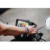 Na zdjęciu widoczny jest tablet zamontowany na motocyklu, na ekranie którego wyświetlane są kolorowe ikony aplikacji. Obok tabletu znajduje się lusterko motocyklowe oraz ręka dotykająca urządzenia.