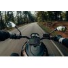 Zdjęcie przedstawia widok z perspektywy kierowcy motocykla jadącego po asfaltowej drodze otoczonej drzewami. Na kierownicy zamontowany jest tablet z widoczną nawigacją, pokazującą mapę i trasę.