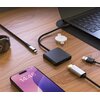 Na drewnianym blacie znajduje się czarny hub z napisem "FIXED", podłączony do laptopa, obok którego leży smartfon z wyświetlaczem pokazującym godzinę 14:48 i datę "Tuesday 4 March". W pobliżu widoczne są różne kable i akcesoria elektroniczne, w tym zegare