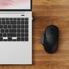 Na zdjęciu widać czarną mysz komputerową obok otwartego laptopa na drewnianym blacie. Klawiatura laptopa ma ciemne klawisze, a ekran wyświetla abstrakcyjny wzór w jasnych kolorach.