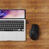 Na drewnianym blacie znajduje się otwarty laptop z widoczną klawiaturą i ekranem, obok którego leży czarna mysz komputerowa. Ekran laptopa wyświetla abstrakcyjny wzór w odcieniach fioletu i różu.