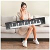 Na zdjęciu znajduje się osoba siedząca na kanapie, trzymająca czarną klawiaturę muzyczną z widocznym napisem "Keyboard MQ 6151L". Klawiatura ma białe i czarne klawisze oraz kilka przycisków i pokręteł na panelu.