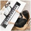 Na zdjęciu widoczny jest czarny keyboard MQ 6151L ustawiony na białym stole, z otwartą książką nutową na stojaku. Obok znajdują się różne przedmioty, takie jak ramka na zdjęcia, kubek z przyborami do pisania i taśma klejąca.