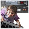 Na zdjęciu widoczny jest fragment elektronicznego keyboardu z napisem "Sound Master MQ-6115L Powerful Music Information System" oraz wyświetlaczem LED z cyframi "98". Obok znajduje się dziecko trzymające klawisze keyboardu.