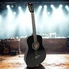 Czarna gitara klasyczna stoi na drewnianej scenie, w tle widoczne są rozmyte światła reflektorów i sprzęt muzyczny. Na główce gitary znajduje się logo z napisem "V-TONE".