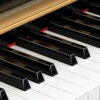 Zbliżenie na klawiaturę pianina cyfrowego z widocznymi czarnymi i białymi klawiszami. Nad klawiszami znajduje się złoty element obudowy.