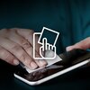 Na zdjęciu widoczna jest dłoń czyszcząca ekran smartfona za pomocą chusteczki. Na obrazie znajduje się również biały symbol przedstawiający dłoń dotykającą ekran.