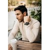 Mężczyzna siedzi przy drewnianym stole na zewnątrz, trzymając kubek z napojem, na jego nadgarstku znajduje się smartwatch AGM MOBILE Legion Czarny. W tle widoczne są rośliny i rozmyte elementy krajobrazu.