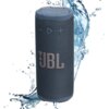 Niebieski głośnik mobilny z widocznym logo "JBL" na siatkowej powierzchni, otoczony rozpryskującą się wodą. Na górze głośnika znajdują się przyciski sterujące w kształcie minus, trójkąta i plusa.