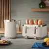 Na zdjęciu znajduje się czajnik i toster w jasnym kolorze z metalicznymi elementami, oba z logo "Russell Hobbs". Toster zawiera cztery kromki pieczywa, a na blacie widoczne są kromki chleba, niebieska serwetka i cytryna.
