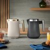 Na zdjęciu znajdują się dwa czajniki elektryczne marki Russell Hobbs, jeden w kolorze beżowym, drugi w czarnym, ustawione na blacie kuchennym. W tle widoczne są elementy dekoracyjne, a na blacie znajdują się filiżanka z herbatą, sok pomarańczowy, talerz z