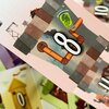 Na zdjęciu widoczna jest karta z gry karcianej z numerem "8" na tle ilustracji przedstawiającej rury i zieloną twarz w słoiku. W tle znajdują się inne karty z różnymi ilustracjami i numerami.