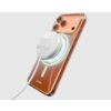 Przezroczyste etui na telefon z widocznym logo "sbs" oraz podłączoną ładowarką MagSafe, która emituje delikatne światło. Telefon ma pomarańczowy tył z trzema aparatami fotograficznymi.