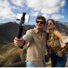 Na zdjęciu widać osobę trzymającą uchwyt selfie z zamocowanym smartfonem, na tle górskiego krajobrazu. Na uchwycie widoczny jest napis "FIXED".