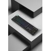 Na zdjęciu znajduje się czarna klawiatura mechaniczna z podświetleniem RGB, umieszczona na szarej, geometrycznej powierzchni. Klawisze są równomiernie podświetlone w różnych kolorach, tworząc efekt tęczy.