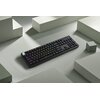 Ciemna klawiatura mechaniczna z podświetleniem RGB leży na jasnym tle, otoczona geometrycznymi bryłami. Klawisze mają różnokolorowe podświetlenie, a jeden z klawiszy wyróżnia się jasnym kolorem.