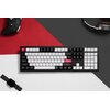 Na zdjęciu znajduje się klawiatura w kolorach czarno-biało-czerwonym, z widocznymi klawiszami oznaczonymi m.in. jako "tab", "caps lock", "shift", "enter", "backspace", "home", "end", "option", "control". W tle widoczne są fragmenty kontrolera do gier, słu