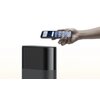 Na zdjęciu widoczny jest czarny, pionowy router oraz ręka trzymająca smartfon z wyświetlonymi ikonami aplikacji. Router ma gładką, zaokrągloną obudowę, a ekran smartfona pokazuje kilka kolorowych ikon.