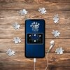 Na zdjęciu widać smartfon z wyświetlaczem pokazującym napis "3D Puzzle Iconics" oraz "PLAYLIST", otoczony elementami puzzli z numerami, leżący na drewnianej powierzchni. Obok telefonu znajduje się biały przewodowy słuchawka.