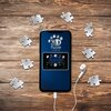Na zdjęciu znajduje się smartfon z wyświetlaczem pokazującym napis "3D Puzzle Iconics" oraz "PLAYLIST", otoczony elementami puzzli z numerami, leżący na drewnianej powierzchni. Obok telefonu widoczne są białe słuchawki przewodowe.