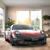 Na zdjęciu znajduje się model samochodu sportowego z puzzli 3D, przedstawiający Porsche 911 GT3 CUP, ustawiony na drewnianym stole w jasnym pomieszczeniu z dużym oknem w tle. Na samochodzie widoczne są napisy "MICHELIN", "CHOPARD" oraz "Mobil 1".