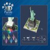 Na zdjęciu znajduje się opakowanie puzzli 3D przedstawiających Statuę Wolności, z widocznym napisem "3D Puzzle Iconics" oraz grafiką pokazującą różne tryby podświetlenia LED w różnych kolorach. Obok znajduje się schemat ilustrujący sposób zmiany kolorów p
