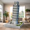 Na zdjęciu znajduje się model 3D Krzywej Wieży w Pizie z puzzli, umieszczony na podstawce z napisem "TORRE PENDENTE DI PISA". W tle widoczny jest jasny pokój z roślinami i sofą.