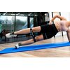 Osoba ćwiczy na niebieskiej macie, używając czarnej gumy do ćwiczeń z napisem "DRFIT". W tle widoczne jest szklane okno z napisem "skills".