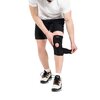 Na zdjęciu widoczny jest stabilizator kolana w kolorze czarnym z otworem na rzepkę, na którym znajduje się napis "DRFIT". Osoba na zdjęciu ma na sobie białą koszulkę, czarne spodenki i białe buty sportowe z czarnymi i pomarańczowymi elementami.