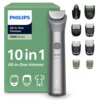 Na zdjęciu znajduje się trymer PHILIPS Multigroom Seria 5000 MG5931/15 wraz z różnymi nasadkami, obok zielonego opakowania z napisem "PHILIPS All-in-One Trimmer 5000 Series 10 in 1 All-in-One trimmer". Na trymerze widoczny jest przycisk zasilania oraz nap