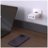 Na zdjęciu widać biały adapter sieciowy podłączony do gniazdka ściennego, obok którego na drewnianym blacie leży ciemny smartfon oraz otwarty laptop z widocznym logo w kształcie jabłka na ekranie. Adapter ma cztery porty USB, w tym jeden zielony.