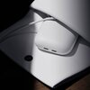 Białe urządzenie z dwoma portami USB-C leży na białej powierzchni, obok widoczny jest biały kabel. Na powierzchni znajduje się czarny, okrągły element.