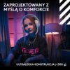 Na zdjęciu widoczna jest osoba nosząca białe, bezprzewodowe słuchawki nauszne, siedząca w pomieszczeniu oświetlonym lampą stojącą, z zasłonami w tle. Na górze zdjęcia znajduje się tekst: "ZAPROJEKTOWANY Z MYŚLĄ O KOMFORCIE", a na dole: "ULTRALEKKA KONSTRU