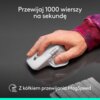 Na zdjęciu widać dłoń trzymającą ciemnoszarą mysz komputerową na ciemnym tle, z widocznym napisem: "Przewijaj 1000 wierszy na sekundę" oraz "Z kółkiem przewijania MagSpeed". W tle znajduje się fragment klawiatury.