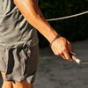 Na zdjęciu widoczna jest ręka trzymająca skakankę z napisem "CENTR" na uchwycie. Osoba ma na sobie szare spodenki i koszulkę, a w tle widać rozmytą zieleń.