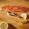 Na drewnianej desce do krojenia leży filet z łososia, obok którego znajduje się metalowa pęseta z napisem "FISKARS Functional Form". Wokół rozmieszczone są plasterki cytryny.