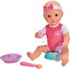 Na zdjęciu znajduje się lalka w różowym ubranku z białymi serduszkami i napisem "New Born Baby", siedząca z akcesoriami: smoczkiem, butelką, talerzykiem i łyżeczką. Lalka ma na głowie opaskę z kokardką.