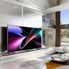 Na zdjęciu znajduje się nowoczesny salon z dużym telewizorem wyświetlającym kolorową grafikę abstrakcyjną. Wnętrze jest eleganckie, z jasnymi ścianami, dużymi oknami i nowoczesnymi meblami.