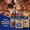 Na zdjęciu widoczne są trzy opakowania kawy Prima z napisami: "Aroma Intenso", "Aroma Italiano" i "Aroma Gold", na tle zbliżenia na ziarna kawy. W lewym dolnym rogu znajduje się tekst: "Poczuj świeżość aromatu ziaren".