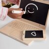 Drewniana zabawka w kształcie laptopa z narysowaną kredą uśmiechniętą buźką na ekranie oraz drewniany telefon z narysowanym sercem. Obok widoczna jest ręka trzymająca kredę.