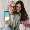 Na zdjęciu widoczny jest smartfon z aplikacją pokazującą wagę 63,80 kg, trzymany przez osobę w okularach. W prawym dolnym rogu znajduje się logo "ALPHA".