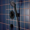 Czarny matowy zestaw prysznicowy zamontowany na ścianie wyłożonej niebieskimi płytkami z pomarańczowymi fugami. Na okrągłym panelu widoczny jest napis "hansgrohe".