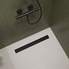 Na zdjęciu znajduje się odpływ liniowy w łazience z ciemnozielonymi płytkami na ścianie i jasną podłogą. Na odpływie widoczny jest napis "hansgrohe".