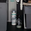 Na zdjęciu znajduje się wnętrze szafki z widocznym wkładem filtrującym marki Hansgrohe oraz przezroczystą butelką z rozpylaczem. Na wkładzie widnieje napis: "hansgrohe claro aktiv kohle filter".
