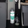Na zdjęciu znajduje się butelka z napisem "hansgrohe claro by BWT SPORT" oraz przezroczysta butelka z rozpylaczem, umieszczone w ciemnym otoczeniu z widocznymi elementami instalacji wodnej. W tle widoczne są szare urządzenia i złożone ręczniki.