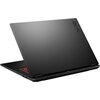 Na zdjęciu widoczny jest czarny laptop z logo "TUF" na pokrywie, częściowo otwarty, z widoczną czerwoną klawiaturą. Laptop ma matowe wykończenie i nowoczesny design.