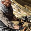 Mężczyzna w okularach ochronnych i rękawicach trzyma piłę akumulatorową, przycinając gałęzie drzewa. Na piłę widoczny jest napis "WORX" oraz oznaczenia techniczne.
