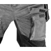 Zdjęcie przedstawia fragment spodni roboczych z materiału denim, z widoczną kieszenią zapinaną na zamek błyskawiczny oraz rzepy. Spodnie mają kontrastowe wstawki materiałowe i wyraźne szwy.