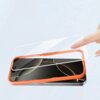 Na zdjęciu widoczny jest smartfon z nałożoną pomarańczową ramką, nad którym unosi się przezroczyste szkło hartowane. W tle widać jasne, jednolite tło, a po prawej stronie znajduje się dłoń wskazująca na szkło.