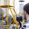 Na zdjęciu widać osobę trzymającą kamerę termowizyjną marki Guide, skierowaną w stronę przemysłowych konstrukcji z żółtymi elementami. Na kamerze widoczne są napisy: "Guide" oraz "PL 550".